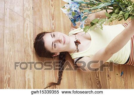 Stock Photography - High angle view of a young woman lying on the floor and holding up a bunch of flowers. Fotosearch
