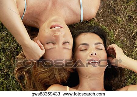 Stock Image - High angle view of two mid adult women lying on the grass with their eyes closed. Fotosearch