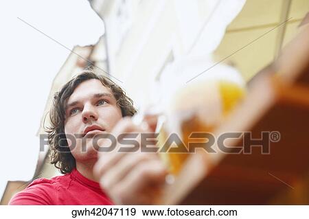 Low angle view of a young man holding a glass of beer View Large Photo Image Stock Photo - Low angle view of a young man holding a glass of beer . Fotosearch