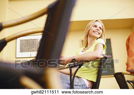 Low angle view of a young woman sitting on a chair and smiling View Large Photo Image Stock Image - Low angle view of a young woman sitting on a chair and smiling . Fotosearch