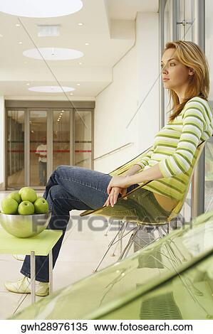 Low angle view of a young woman sitting on a chair View Large Photo Image Stock Photography - Low angle view of a young woman sitting on a chair. Fotosearch
