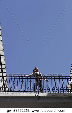Low angle view of a young woman standing in the balcony of a building View Large Photo Image Stock Image - Low angle view of a young woman standing in the balcony of a building . Fotosearch