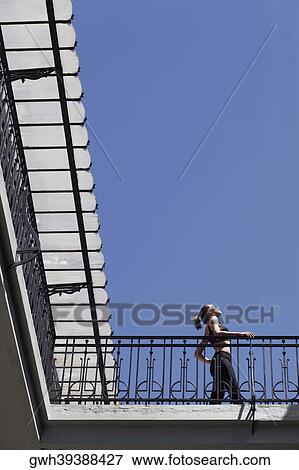 Stock Photo - Low angle view of a young woman standing in the balcony of a building . Fotosearch