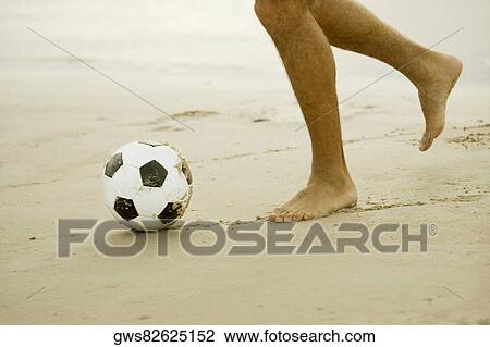 Stock Image - Low section view of a man playing soccer on the beach. Fotosearch