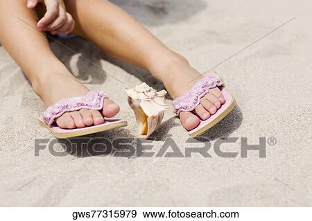 Stock Photo - Low section view of a person's feet near a conch shell. Fotosearch