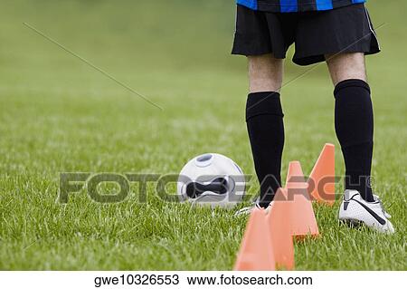 Stock Image - Low section view of a soccer player practicing dribbling. Fotosearch