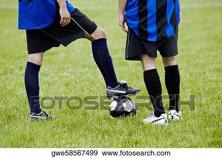 Low section view of a soccer player resting his foot on a soccer ball with another player standing beside him View Large Photo Image Stock Photo - Low section view of a soccer player resting his foot on a soccer ball with another player standing beside him. Fotosearch