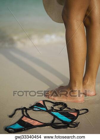 Picture - Low section view of a woman standing on the beach near a bikini. Fotosearch