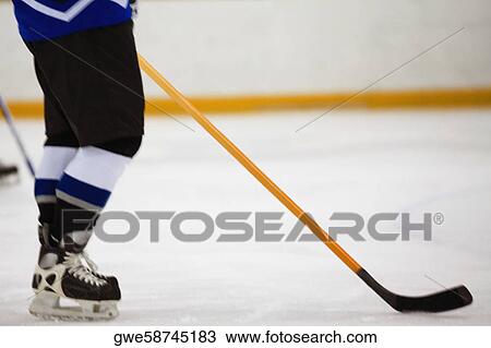 Stock Image - Low section view of an ice hockey player holding an ice hockey stick. Fotosearch