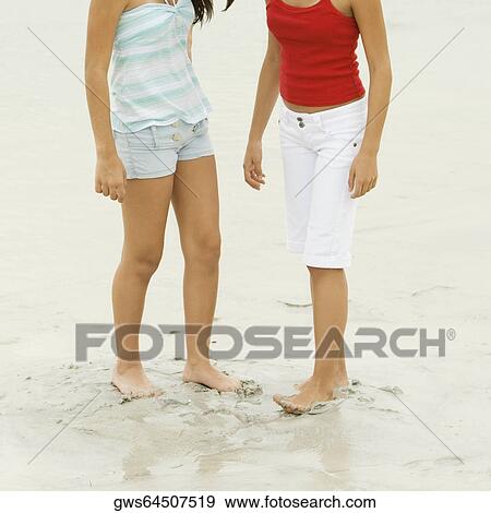 Stock Photo - Low section view of two girls standing on the beach. Fotosearch
