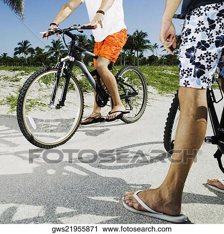 Stock Image - Low section view of two men with their bicycles on a road. Fotosearch