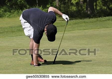 Stock Photography - Man putting his hand in a hole on a golf course. Fotosearch
