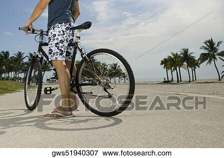 Stock Photo - Man standing with his bicycle on the road. Fotosearch