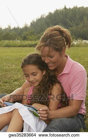 Mature woman and her daughter reading a book in the park View Large Photo Image Picture - Mature woman and her daughter reading a book in the park. Fotosearch