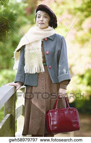 Mature woman standing holding a bag View Large Photo Image Stock Photo - Mature woman standing holding a bag . Fotosearch