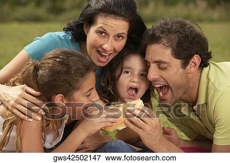 Stock Photo - Mid adult man and a young woman eating a burger with their two daughters. Fotosearch