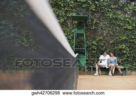 Mid adult man and a young woman sitting on a bench on a tennis court View Large Photo Image Stock Photo - Mid adult man and a young woman sitting on a bench on a tennis court. Fotosearch