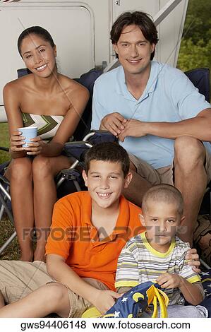 Mid adult man and a young woman sitting with their two children and smiling View Large Photo Image Stock Photo - Mid adult man and a young woman sitting with their two children and smiling. Fotosearch