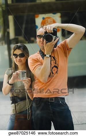 Stock Photograph - Mid adult man and a young woman taking photographs. Fotosearch