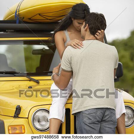 Mid adult man embracing a young woman sitting on the bonnet of a jeep View Large Photo Image Stock Photo - Mid adult man embracing a young woman sitting on the bonnet of a jeep. Fotosearch