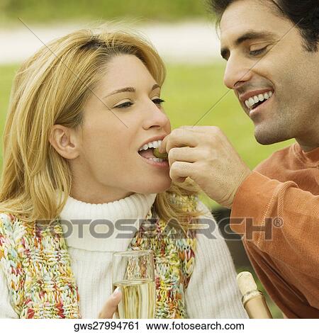 Stock Image - Mid adult man feeding grapes to a young woman. Fotosearch