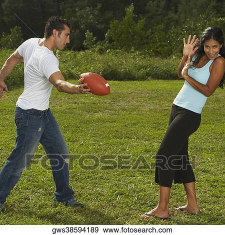 Mid adult man standing holding a football in front of a young woman View Large Photo Image Stock Photo - Mid adult man standing holding a football in front of a young woman. Fotosearch