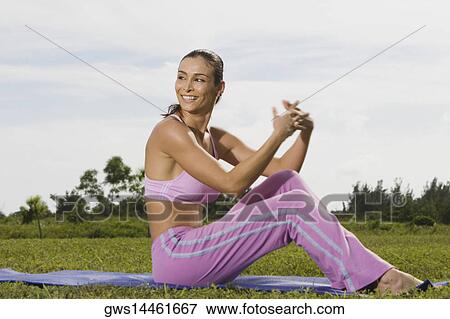 Stock Photo - Mid adult woman sitting on an exercising mat with her hands clasped. Fotosearch