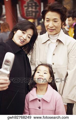 Stock Photo - Mid adult woman with her mother and her daughter taking a photograph of themselves . Fotosearch