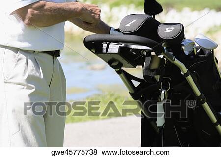 Stock Photo - Mid section view of a man putting a golf club into a golf bag. Fotosearch