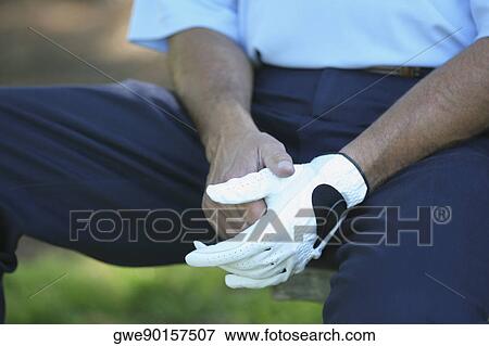 Mid section view of a man sitting on the bench wearing a golf glove View Large Photo Image Stock Photo - Mid section view of a man sitting on the bench wearing a golf glove. Fotosearch