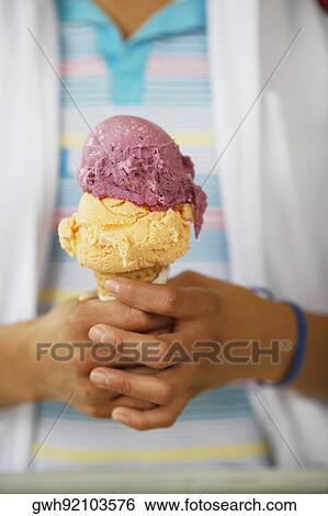 Stock Photograph - Mid section view of a person holding an ice-cream. Fotosearch