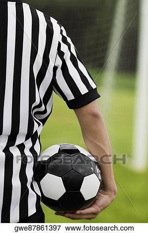 Stock Photo - Mid section view of a referee carrying a soccer ball. Fotosearch