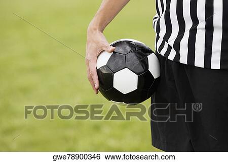 Stock Photograph - Mid section view of a referee holding a soccer ball. Fotosearch