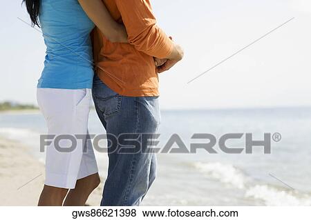 Mid section view of a woman embracing a man from behind on the beach View Large Photo Image Stock Photo - Mid section view of a woman embracing a man from behind on the beach. Fotosearch