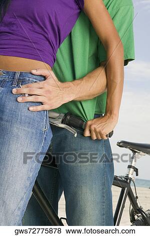 Stock Photo - Mid section view of a young couple standing with a bicycle on the beach. Fotosearch