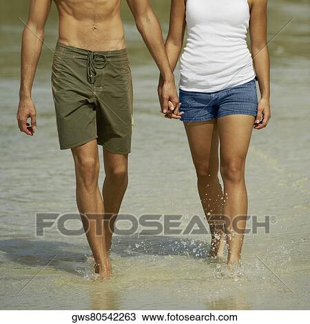 Mid section view of a young man and a teenage girl holding hands and walking on the beach View Large Photo Image Stock Image - Mid section view of a young man and a teenage girl holding hands and walking on the beach. Fotosearch