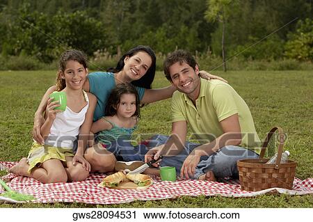 Stock Image - Parents and their two daughters sitting on a picnic blanket. Fotosearch