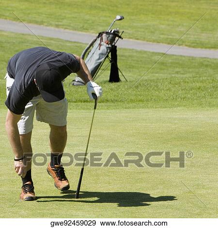 Stock Photo - Person bending holding a golf ball and a golf club. Fotosearch
