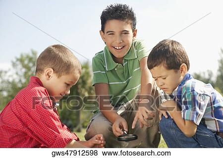 Portrait of a boy holding a magnifying glass with his friends beside him View Large Photo Image Stock Photo - Portrait of a boy holding a magnifying glass with his friends beside him. Fotosearch