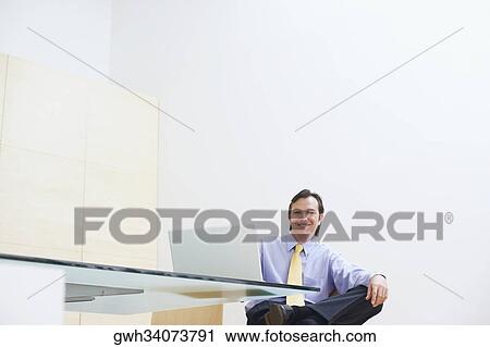 Portrait of a businessman sitting in an office with a laptop in front of him View Large Photo Image Stock Image - Portrait of a businessman sitting in an office with a laptop in front of him. Fotosearch