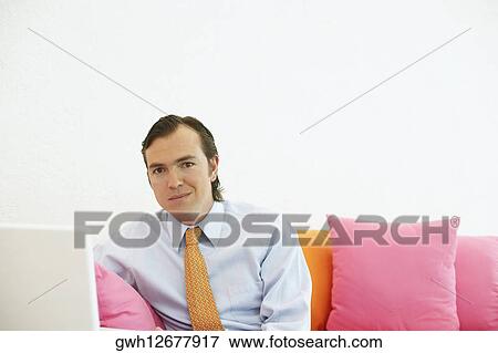 Portrait of a businessman sitting on a couch with a laptop View Large Photo Image Stock Photo - Portrait of a businessman sitting on a couch with a laptop. Fotosearch