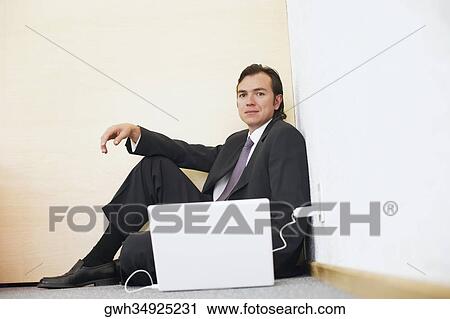 Portrait of a businessman sitting against a wall with a laptop beside him View Large Photo Image Stock Image - Portrait of a businessman sitting against a wall with a laptop beside him. Fotosearch
