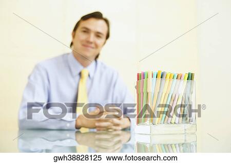 Stock Photography - Portrait of a businessman sitting with felt tip pens in a pen stand in front of him. Fotosearch