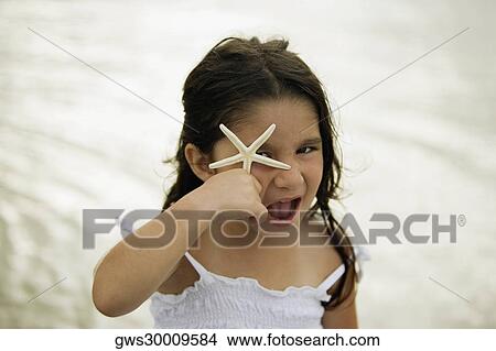 Picture - Portrait of a girl holding a star fish in front of her eye. Fotosearch