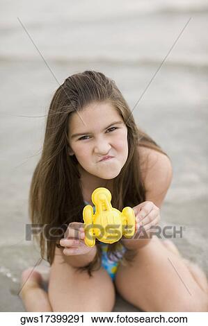 Portrait of a girl kneeling on the beach and holding a toy View Large Photo Image Stock Image - Portrait of a girl kneeling on the beach and holding a toy. Fotosearch