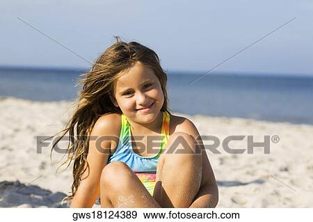 Stock Photo - Portrait of a girl sitting on the beach and smiling. Fotosearch