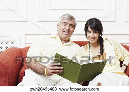 Portrait of a mature man sitting with his daughter on a couch and holding a book View Large Photo Image Stock Image - Portrait of a mature man sitting with his daughter on a couch and holding a book. Fotosearch