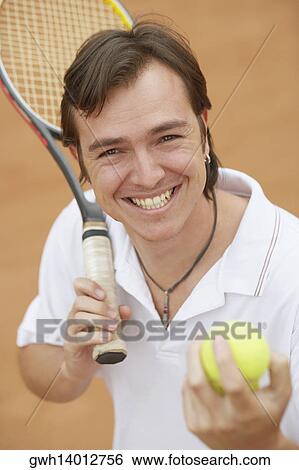 Stock Photograph - Portrait of a mid adult man holding tennis balls and a tennis racket. Fotosearch