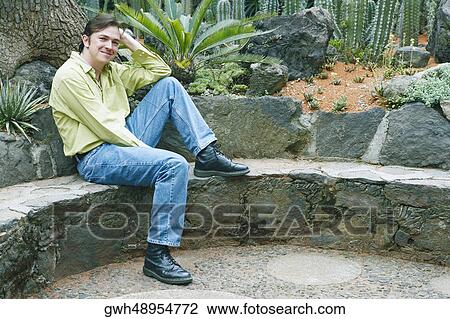 Portrait of a mid adult man sitting on a wall with his hand in his hair View Large Photo Image Stock Image - Portrait of a mid adult man sitting on a wall with his hand in his hair. Fotosearch