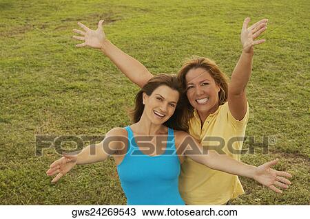Stock Image - Portrait of a mid adult woman and a mature woman standing with their arms outstretched. Fotosearch